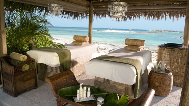 A beachside spa with two massage tables, a wooden bench, and a wicker basket with toiletries. - Dream Now Travel Later (Puerto Plata)