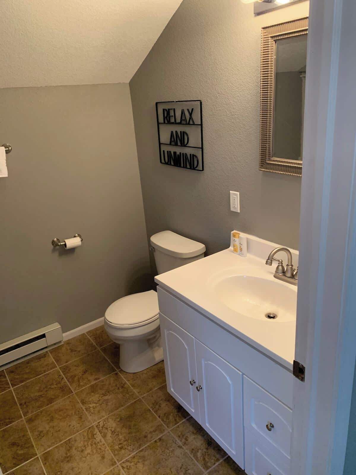 A bathroom with a toilet, sink, and a 'RELAX AND UNMIND' sign on the wall.