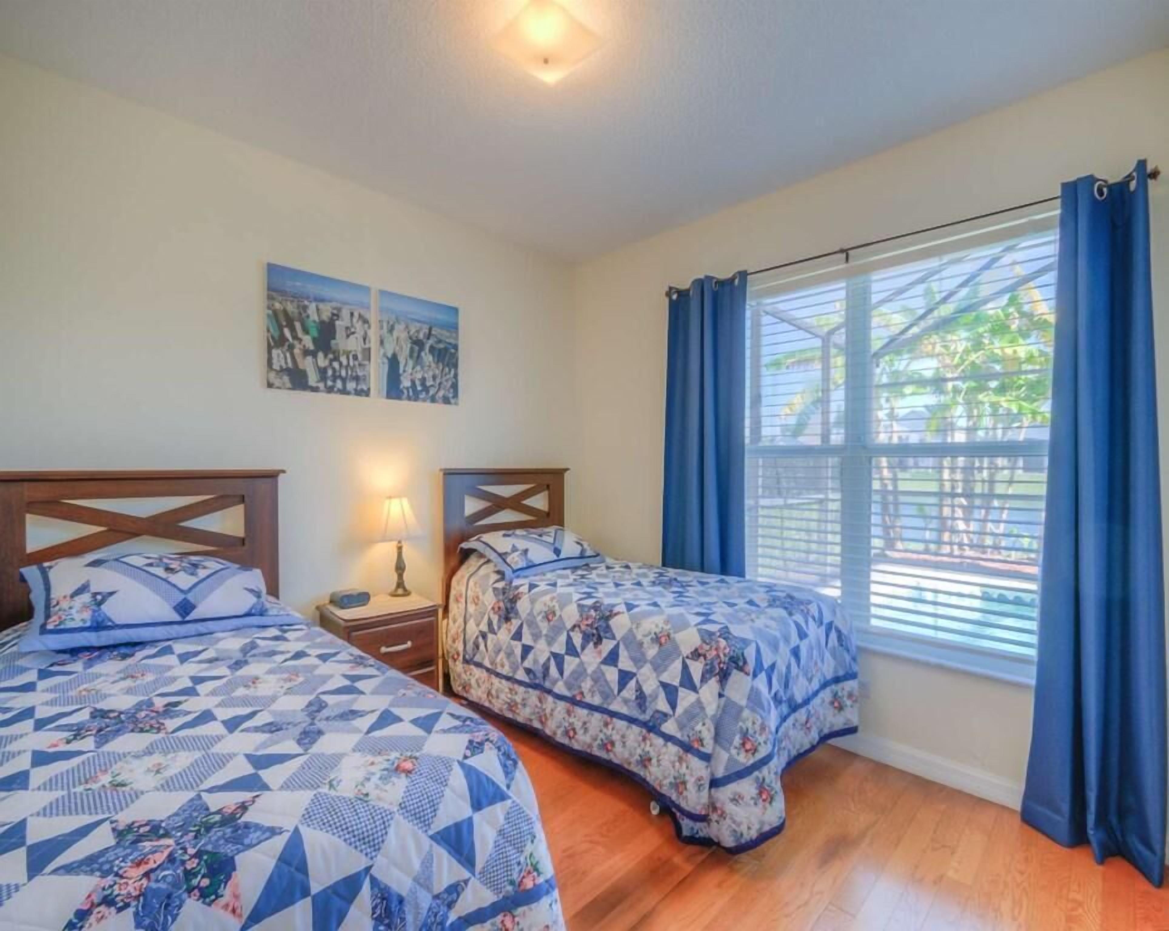 A bedroom with two beds, a nightstand with a lamp, and a window with curtains.