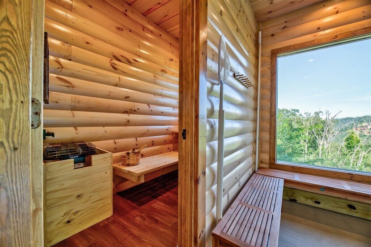 L’intérieur d’un chalet en bois, avec un banc en bois, une petite table et une fenêtre donnant sur un paysage verdoyant.