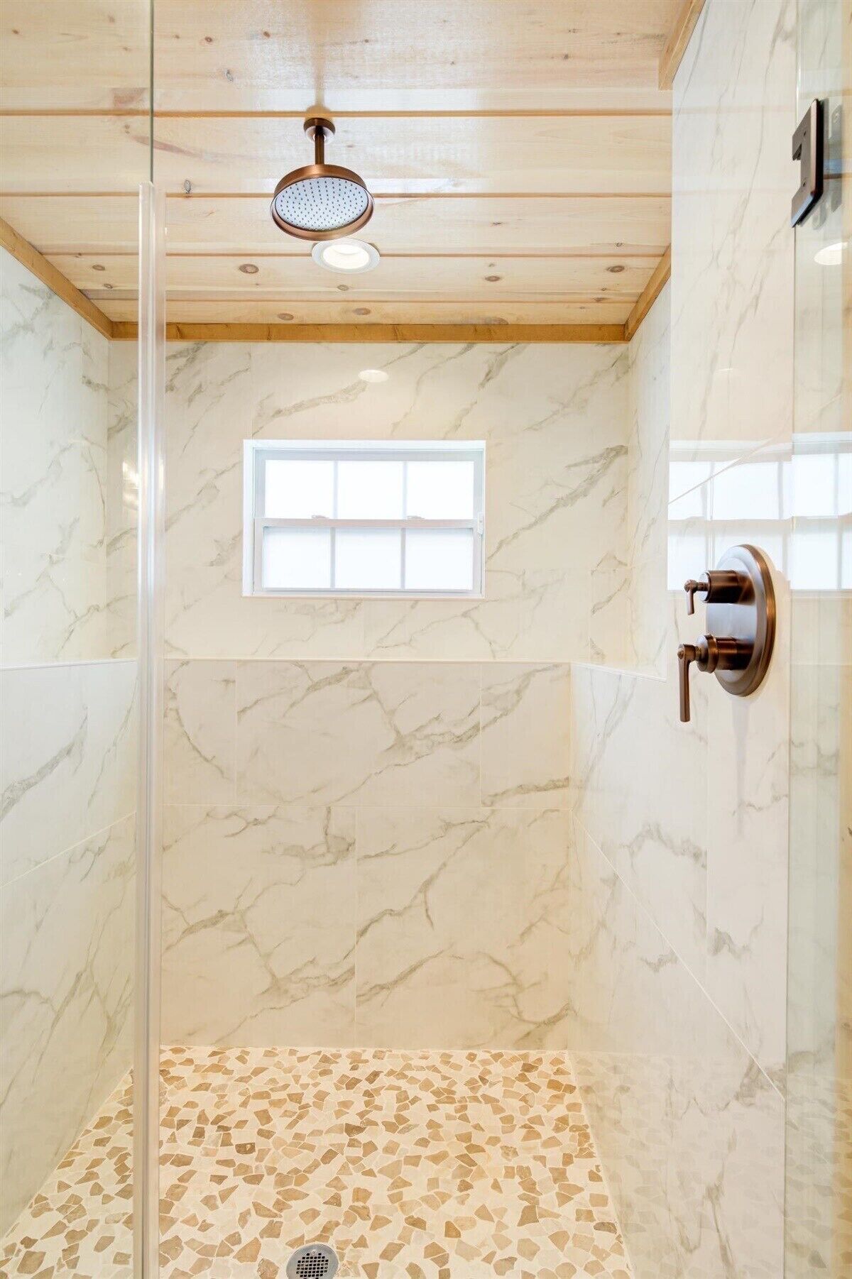 A shower with a glass door, marble walls, and a wooden ceiling.