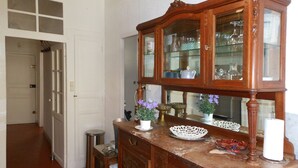 Un armari de fusta amb portes de vidre que conté vaixelles de cuina, un vas blanc amb flors morades i un petit cubell de brossa.