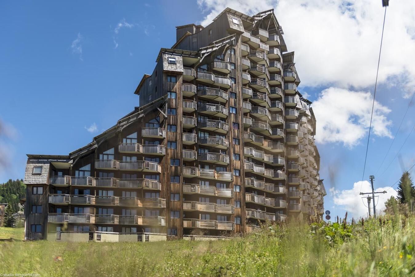 A multi-story building with balconies, likely a hotel or residential complex, set against a clear sky.