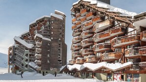 Un centro de esquí cubierto de nieve con edificios modernos de madera, que incluye un telesilla y un restaurante.