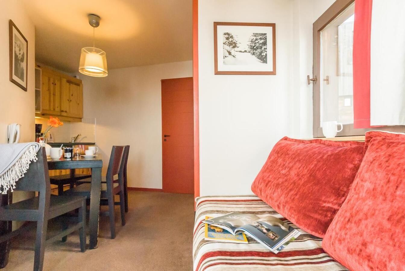 Un salon chaleureux avec un canapé à rayures, une table à manger avec des chaises et un coin cuisine visible à travers une porte ouverte.