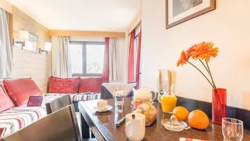 Ett hotellrum med en matplats, en säng med röda kuddar, ett frukostbord med apelsinjuice och en vas med blommor.