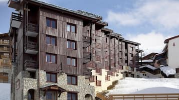 A multi-story hotel with wooden balconies, stone foundation, and a ski slope in the background.