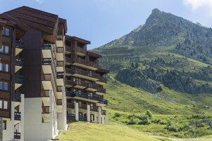 A multi-story hotel with balconies, set against a mountainous backdrop.
