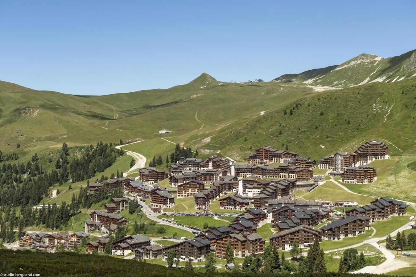 Una località montana con diversi edifici in stile chalet, strade tortuose e sullo sfondo colline e montagne verdi.