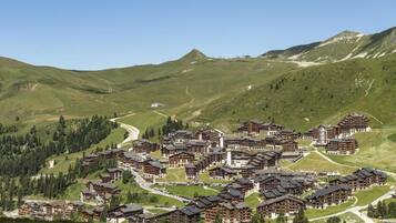 Una località montana con diversi edifici in stile chalet, strade tortuose e sullo sfondo colline e montagne verdi.