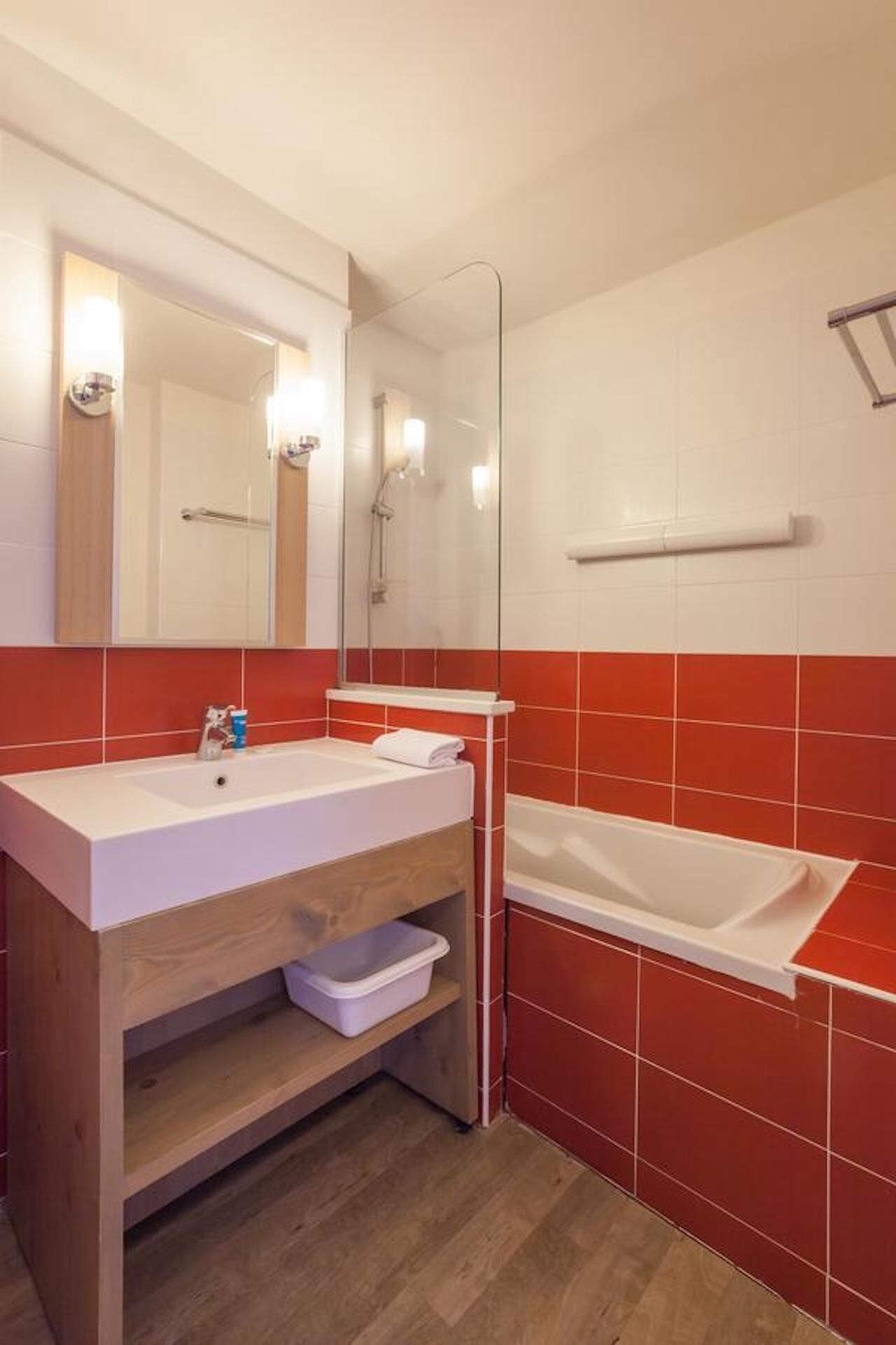 Een badkamer met een houten wastafel, een wit wasbakje, een spiegel, een douche en rode betegelde wanden.