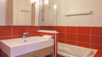Een badkamer met een houten wastafel, een wit wasbakje, een spiegel, een douche en rode betegelde wanden.