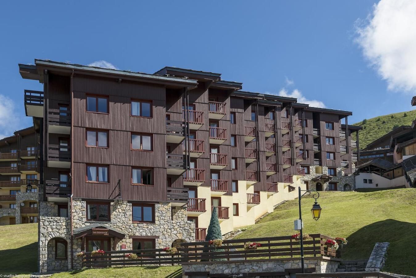 A multi-story hotel with balconies, stone facade, and a ski slope in the background.