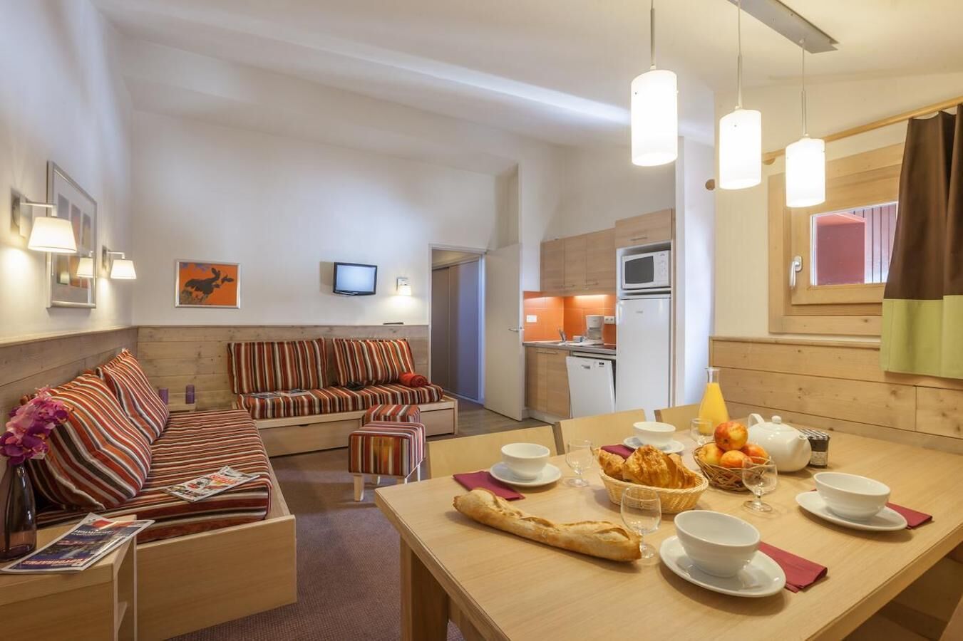 A modern, well-lit living room with a sofa, dining table set with breakfast, and a kitchen in the background.