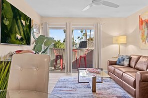 A living room with a sofa, a coffee table, a chair, a TV, and a balcony with red chairs.