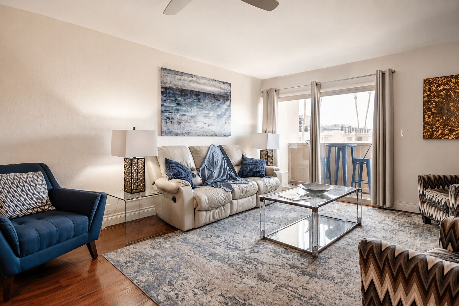 Una sala de estar moderna con un sofá, un sillón y una mesa de centro, que incluye un cuadro de un paisaje urbano y vistas a través de un ventanal grande.