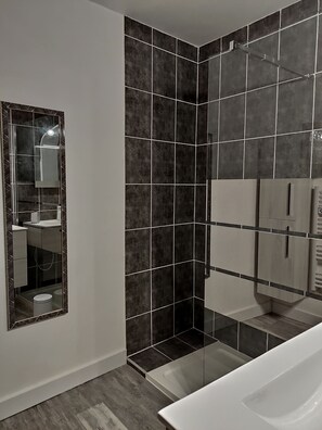 Bathroom features a large mirror, sink, and separate shower area with glass door.