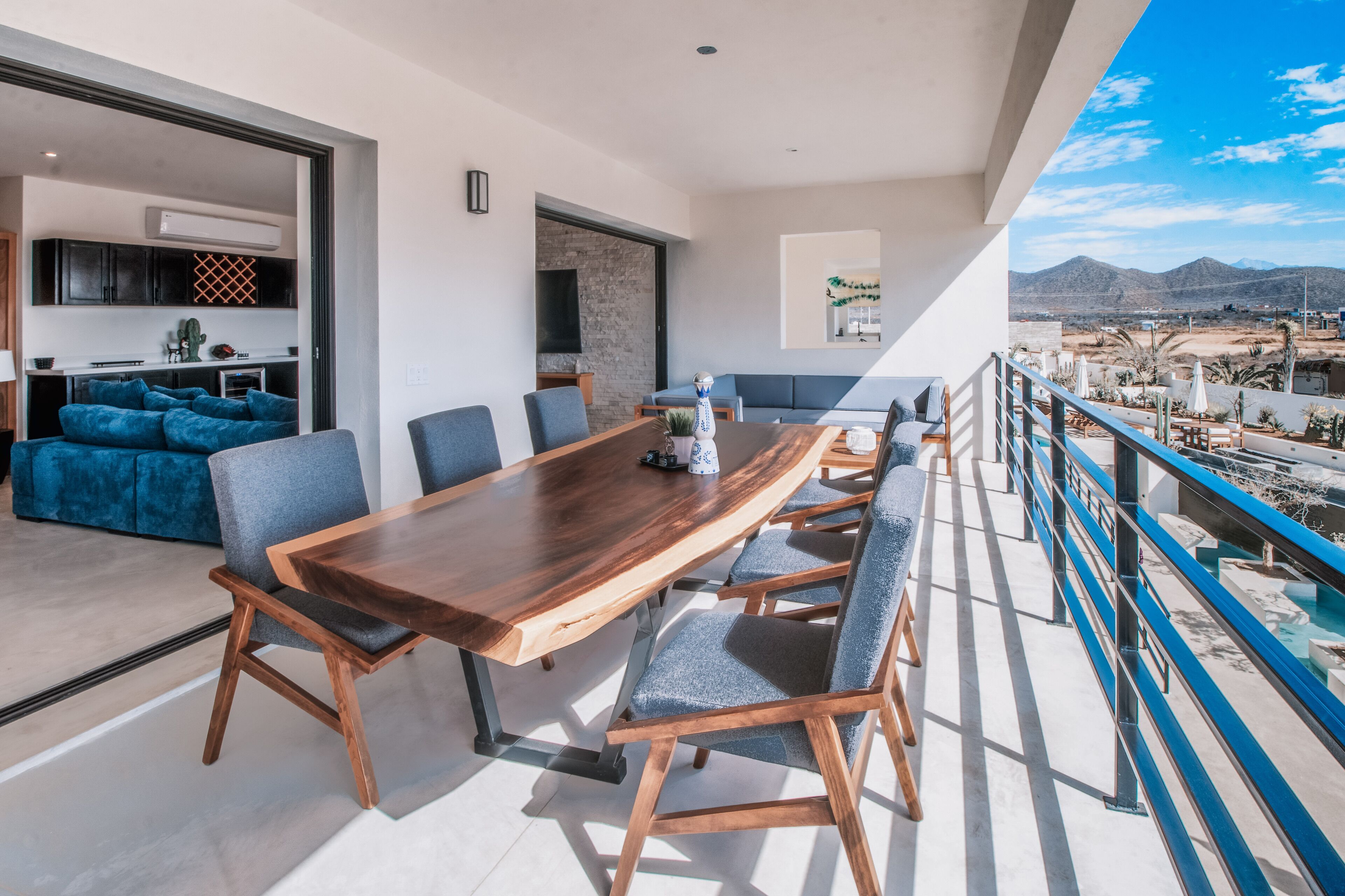 A spacious balcony with a dining area featuring a long wooden table and modern chairs, overlooking a scenic mountainous landscape.