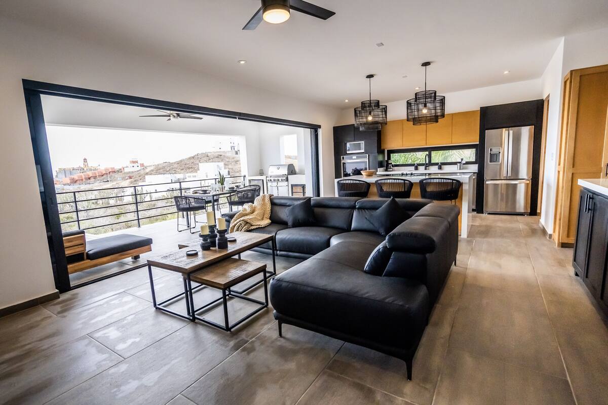 A modern living room with a sectional sofa, a dining table, and a kitchen in the background.