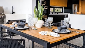 A modern kitchen with a wooden dining table set with black and white plates, bowls, and glassware. - Cerritos Surf Residences (El Pescadero)