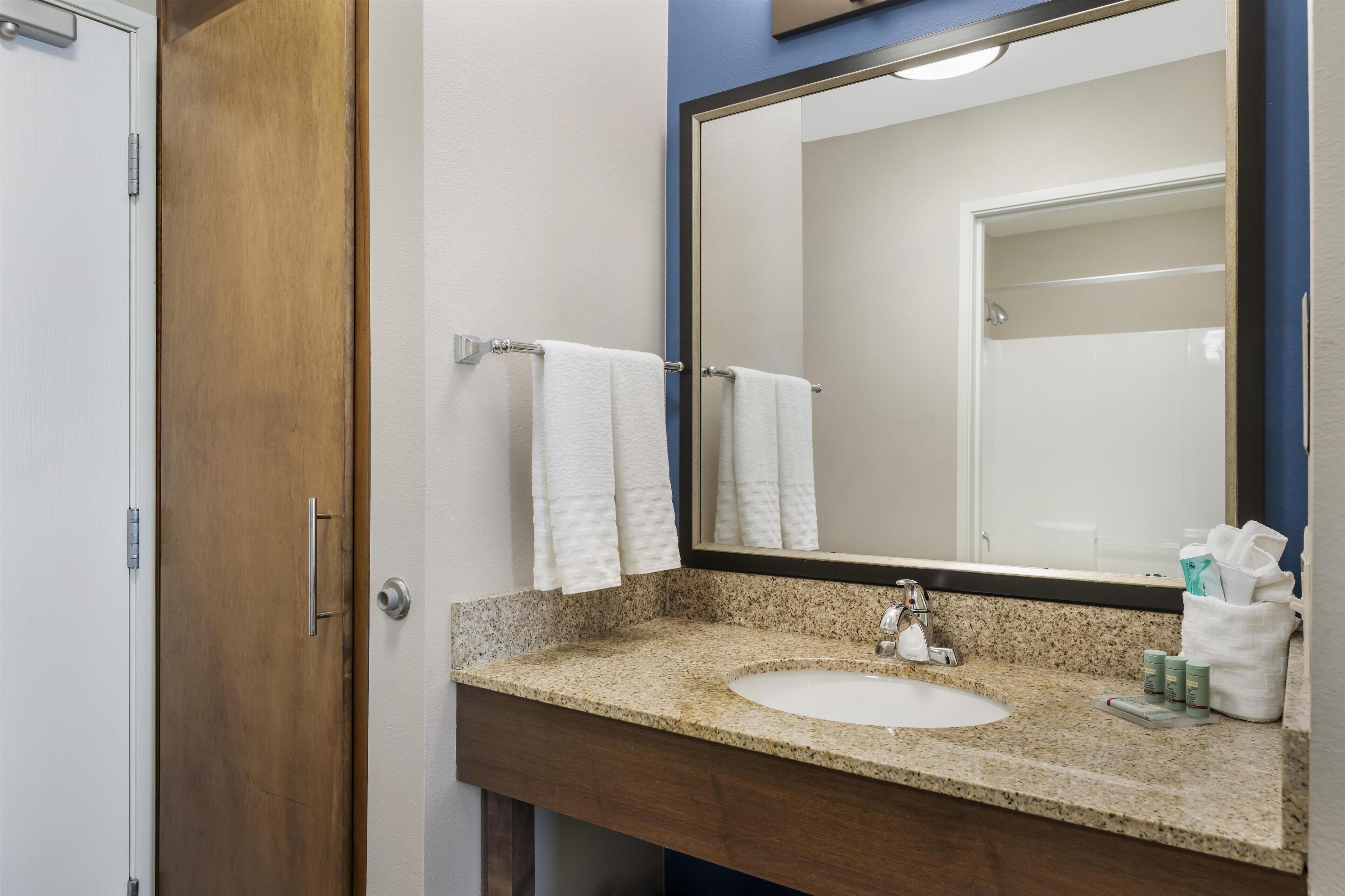 A bathroom with a granite countertop sink, a mirror, and two white towels hanging on a towel rack.
