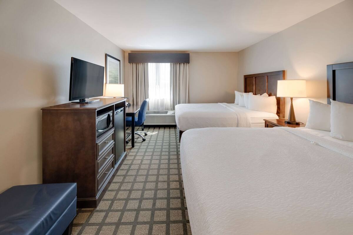 A hotel room with two beds, a desk, a television, and a window with curtains.