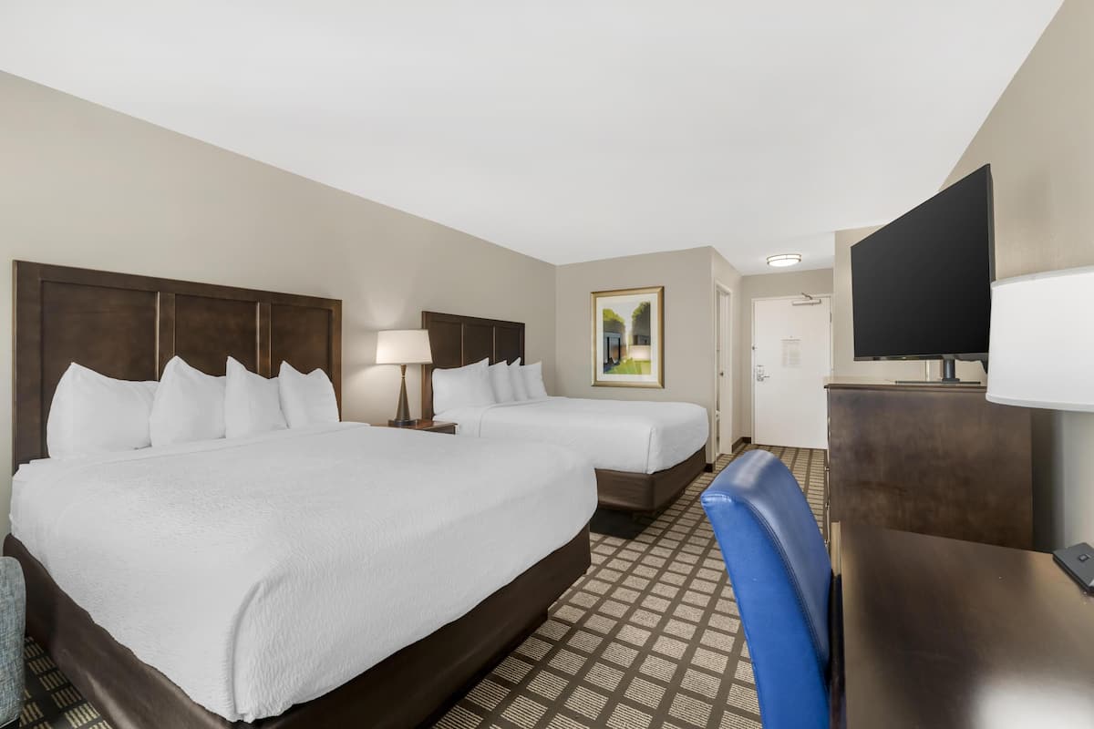 A hotel room with two beds, a desk, a TV, and a painting on the wall.