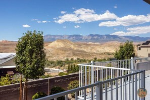 Un balcon avec vue sur les montagnes, un ciel dégagé et un bâtiment au premier plan.