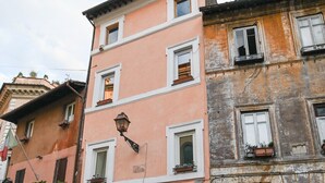 Un immeuble à plusieurs étages avec une devanture de magasin fermée, un scooter garé devant, et une rue pavée.