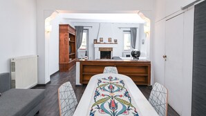 Un salon moderne avec une cheminée, une table à manger agrémentée d’un chemin de table à motifs et une bibliothèque.