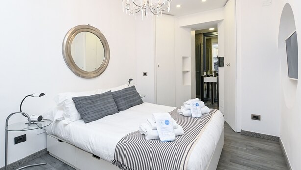 Ein modernes Hotelzimmer mit einem großen Bett, einem runden Spiegel, einer Chandelüster und einem an der Wand befestigten Fernseher.