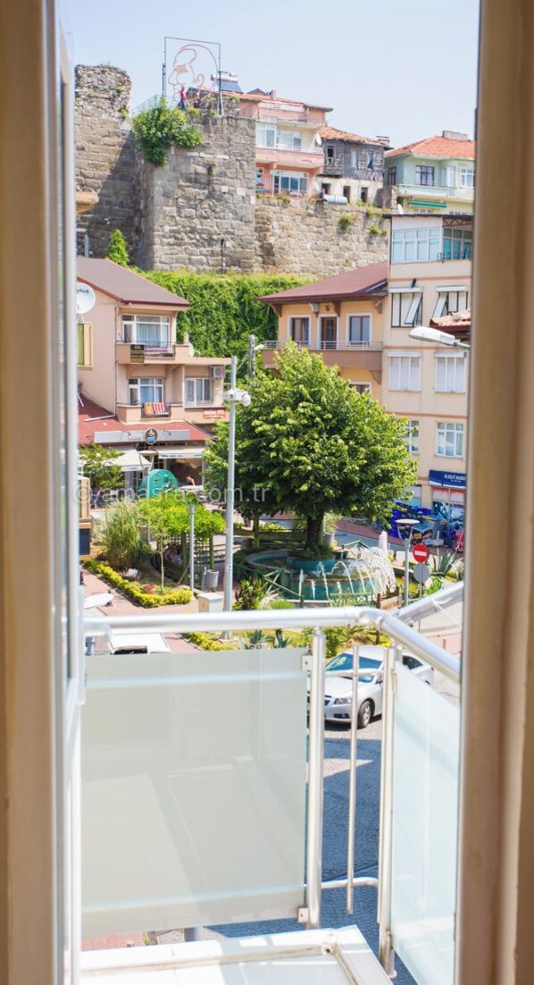A view from a window overlooking a street with buildings, a tree, and a stone wall. - Balkaya Pansiyon (Amasra)