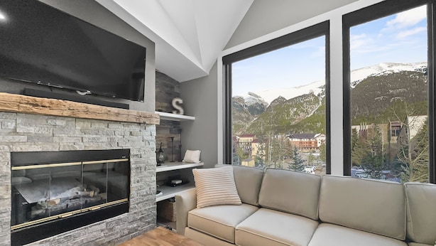 Ein modernes Wohnzimmer mit Kamin aus Stein, einer Couch und einem großen Fenster mit Blick auf die Berge.