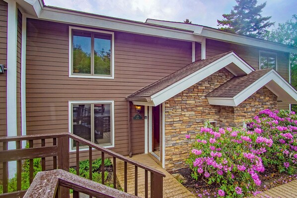 A two-story house with a stone facade and a wooden deck. - Stemwinder 6A, 3 Bedrooms Plus Bonus Sleeping Alcove, 2 1/2 Baths (Snowshoe)