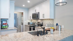 A modern kitchen with white cabinets, a granite countertop, stainless steel appliances, and a pendant light. - Etta Place 102 by Exceptional Stays (Telluride)
