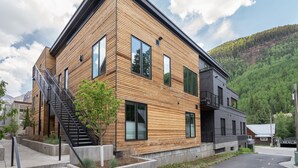Un edificio moderno a due piani con facciata in legno, ampie finestre e una scala che conduce al piano superiore.