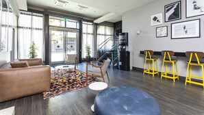 A modern lobby with a leather sofa, a colorful rug, a staircase, and yellow bar stools. - Hotel EPIK (San Francisco)