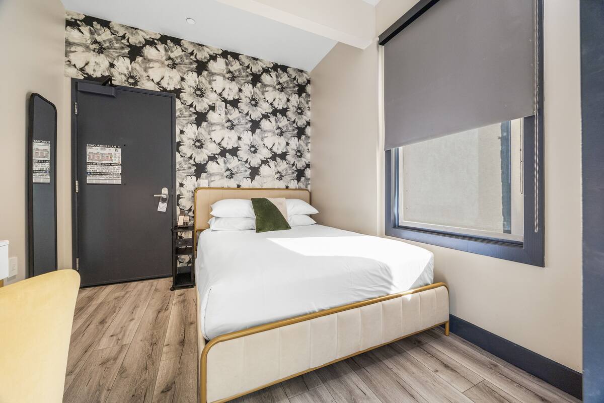 A bedroom with a bed, a door, a window, and a wall with a floral pattern.