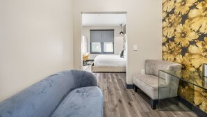 A modern hotel room with a grey sofa, a glass table, and a bed with a grey headboard. - Hotel EPIK (San Francisco)