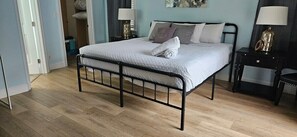 Une chambre à coucher avec un lit en métal, une couvre-lit blanche et deux tables de chevet avec des lampes.