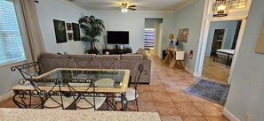 A living room with a glass-top coffee table, a sofa, a television, and a ceiling fan. - Private Hot Tub, 3 Bdrm 3 Bath 1 Mi. To Beach (Lake Worth)