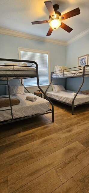 Una habitación con dos literas, un ventilador de techo, una ventana con persianas y un cuadro en la pared.