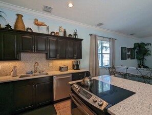 Una cocina moderna con gabinetes oscuros, encimera de granito, horno empotrado y cafetera.
