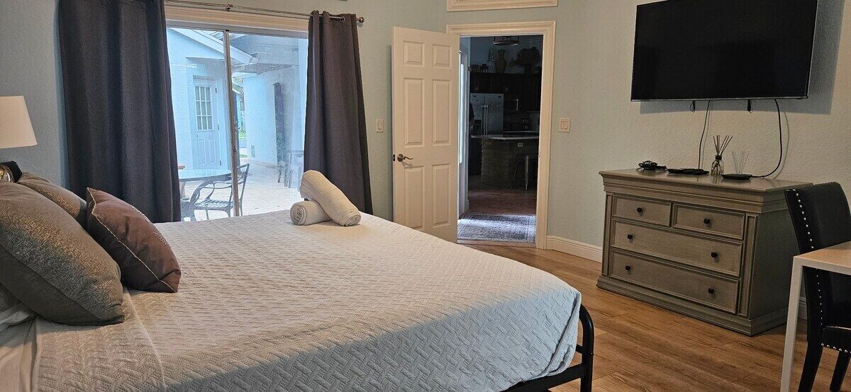 A bedroom with a bed, a dresser, a television, and a door leading to a balcony.