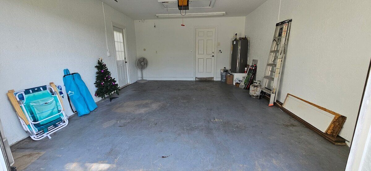 A garage with a concrete floor, a white door, a small Christmas tree, a fan, and a ladder.