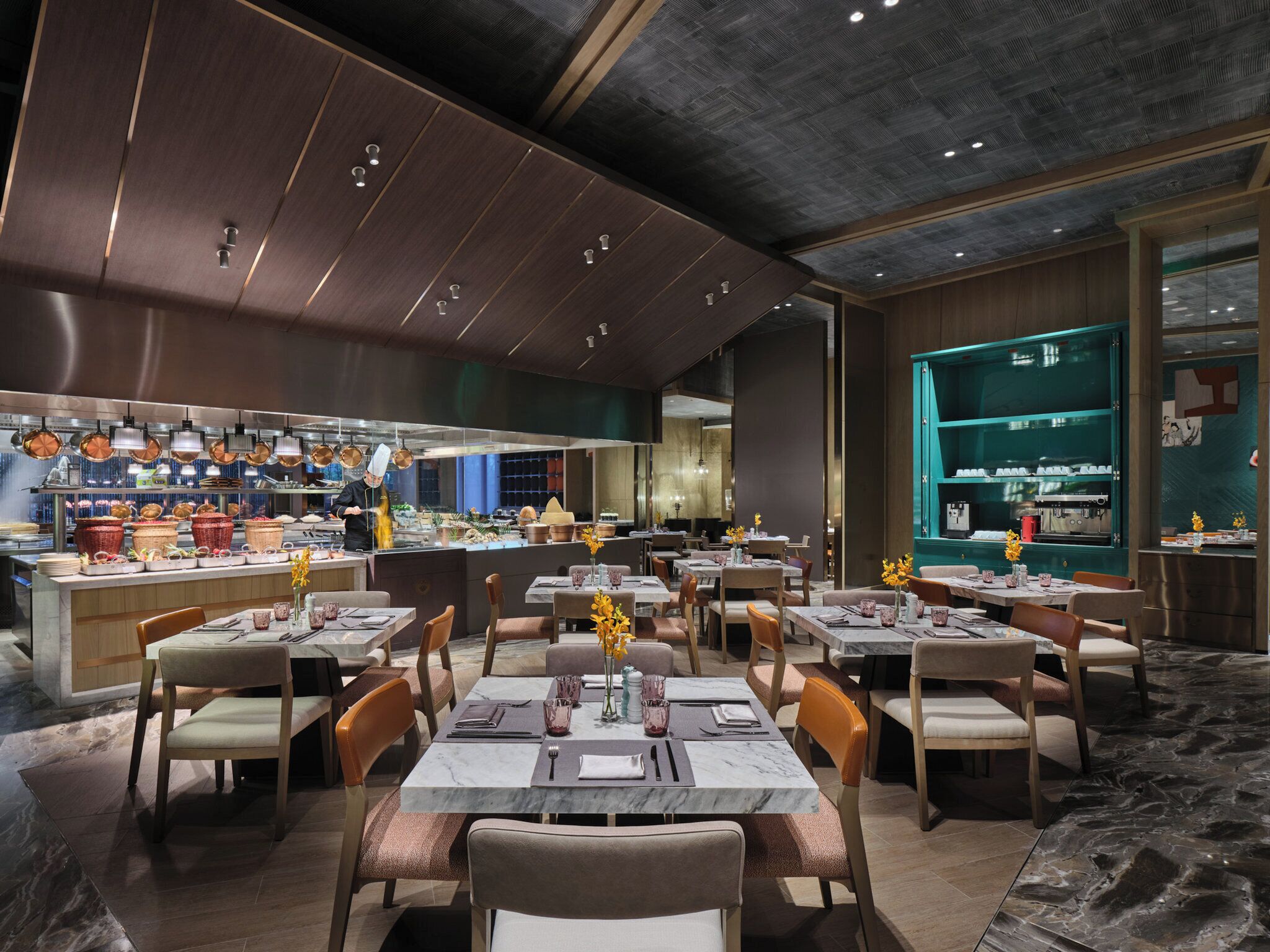 Un restaurante moderno con varias mesas y sillas, una zona de cocina y una vitrina con productos.