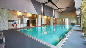 Een binnenzwembad met helder water, omgeven door muren met structuur en moderne verlichting.