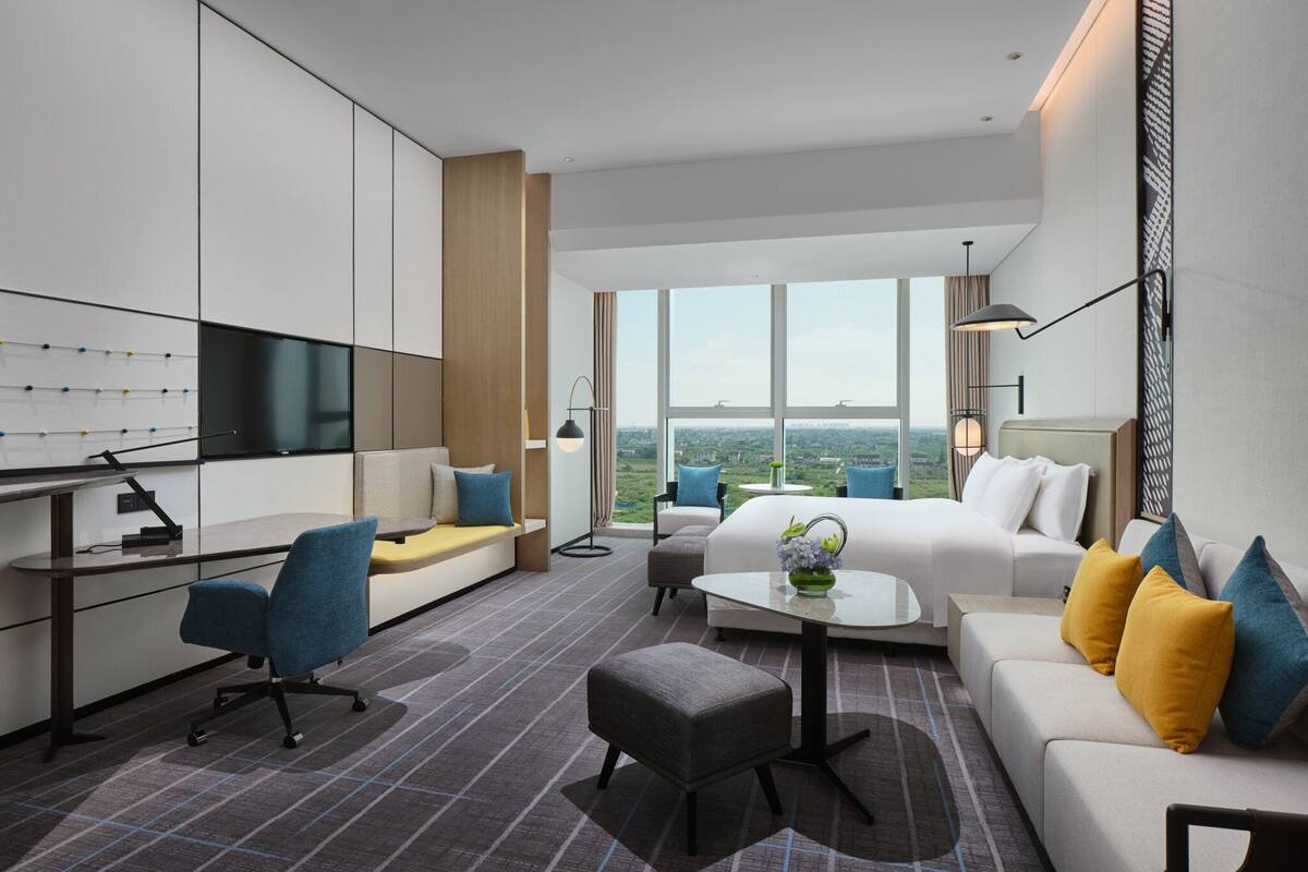 A modern living room with a large window, a sofa, a desk, and a chair.