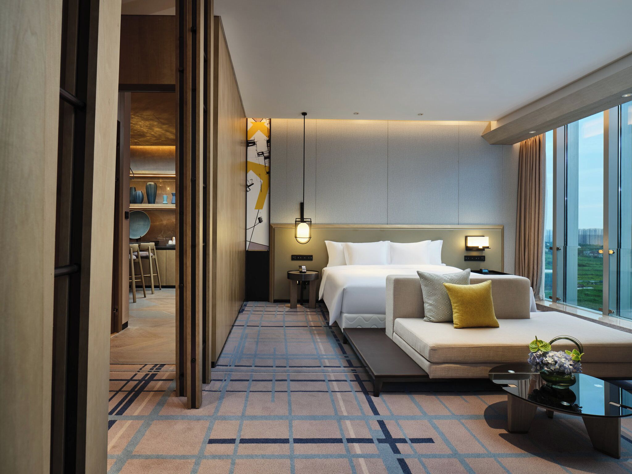 A modern hotel room with a bed, sofa, and a view of the city.