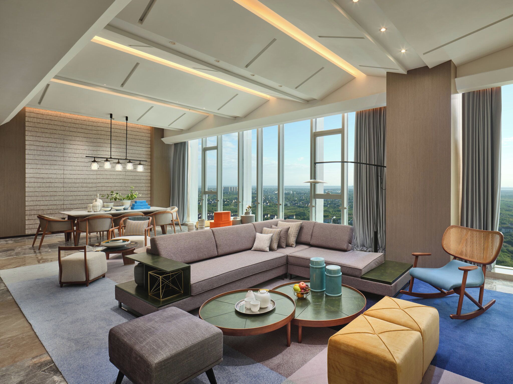 A modern living room with a sectional sofa, a dining area with a table and chairs, and a large window offering a city view.